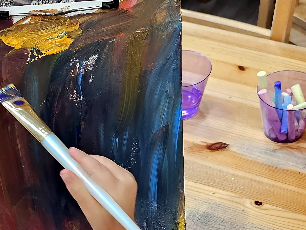 Detalle de una mano aplicando pintura sobre una obra infantil.